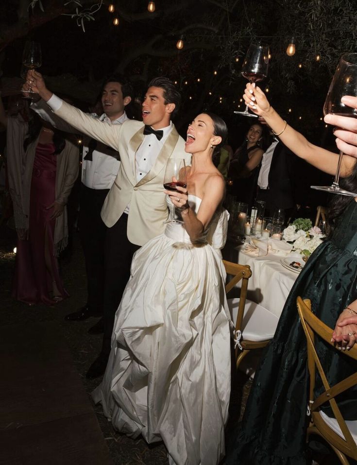 Newlyweds raising their glasses beneath string lights